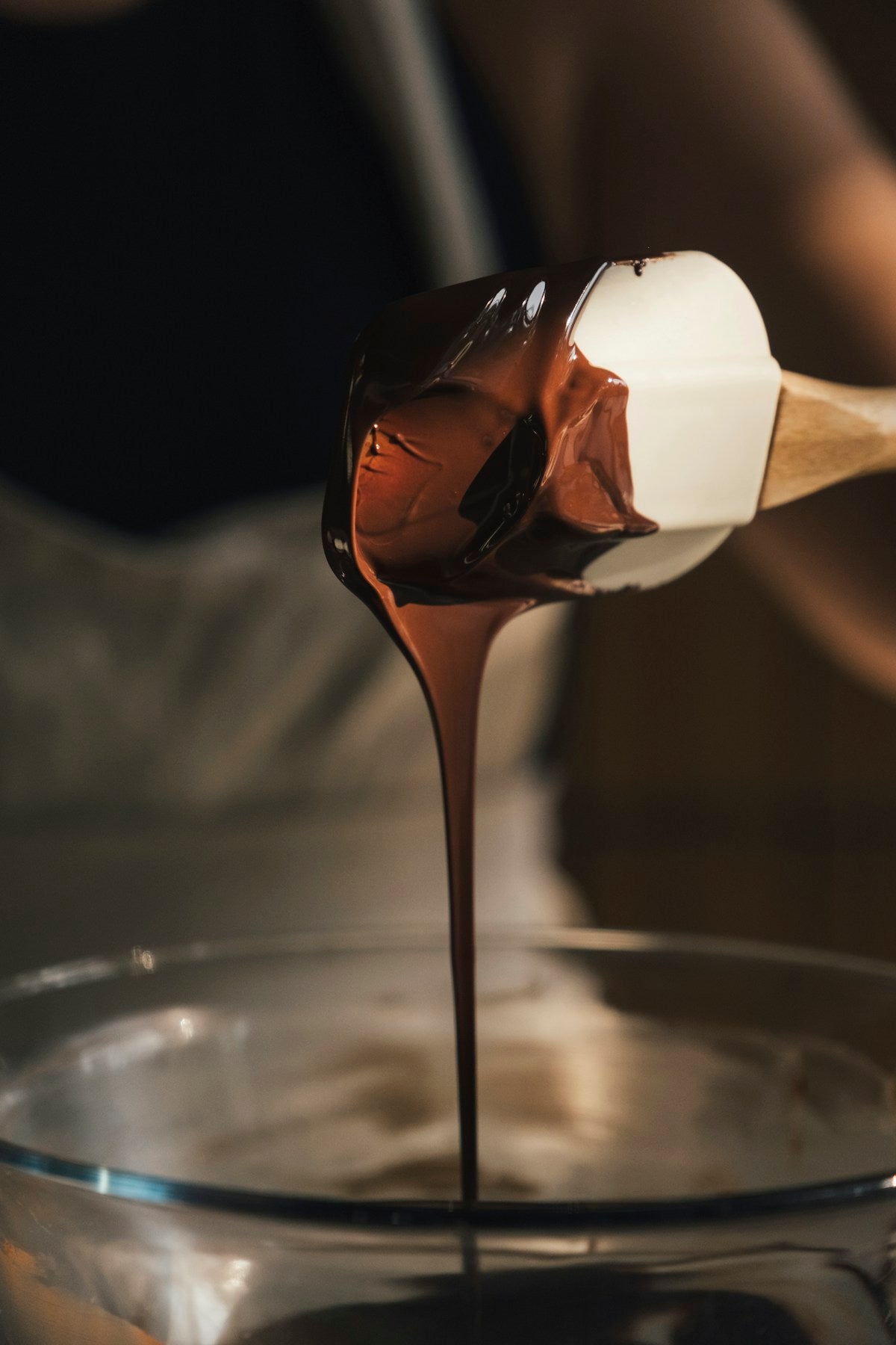 Melted chocolate dripping from a spatula into a bowl, artisan bean-to-bar process